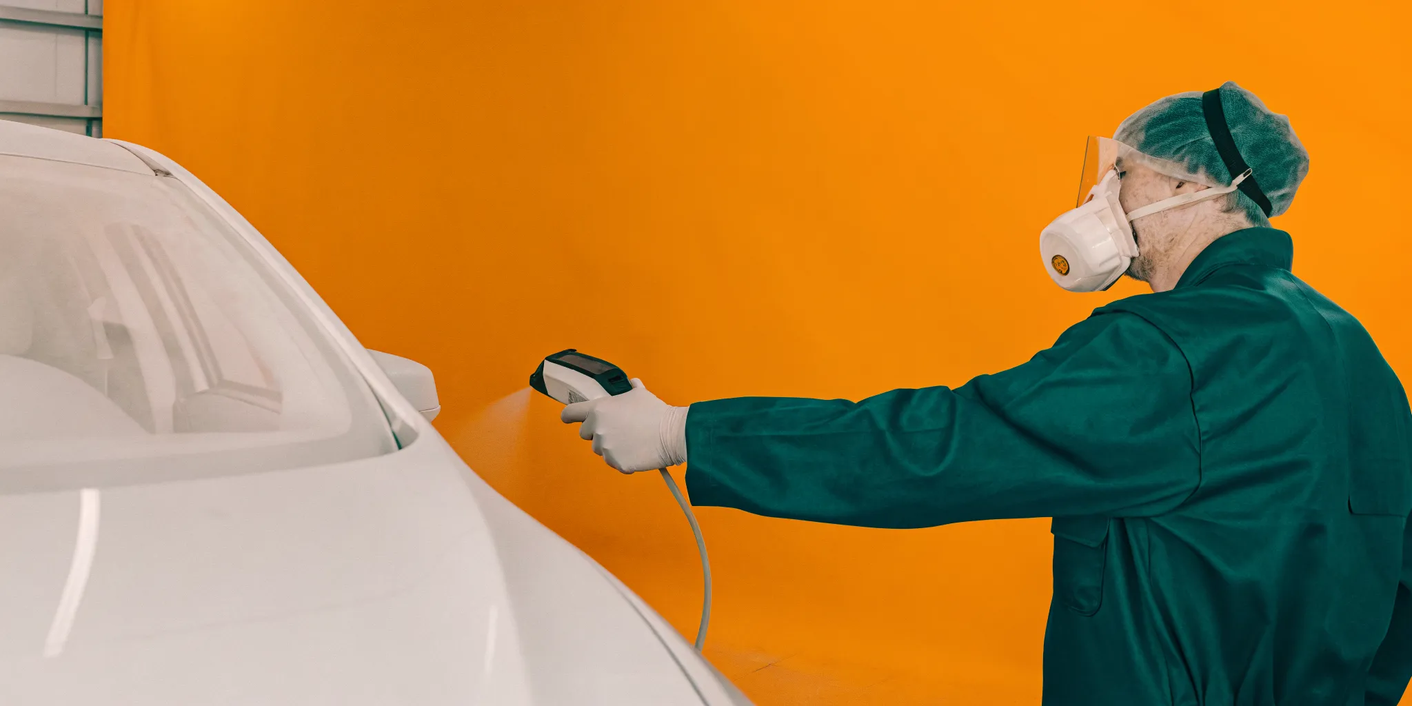 Technician using handheld spectrophotometer to scan car paint color matching in a professional auto body shop